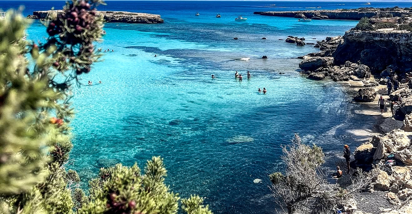 Glassy turquoise water over a pale seabed at the Blue Lagoon on the Akamas peninsula with excursion boats at anchor