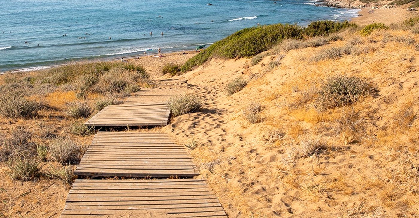 Lara Bay on the Akamas peninsula: a timber boardwalk over low dunes leading down to a wide undeveloped bay with bare hills behind